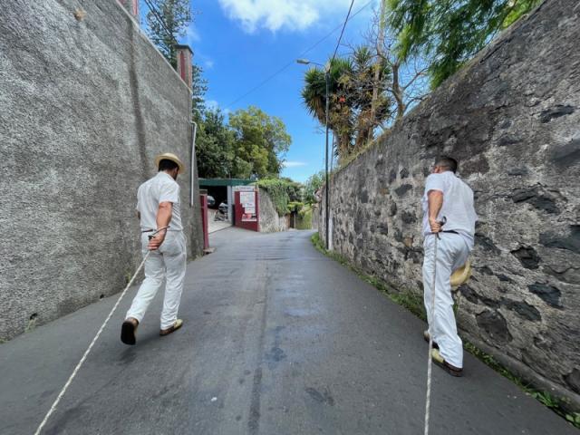 Dva muži na ceste ťahajúci sane v meste Funchal, Madeira.